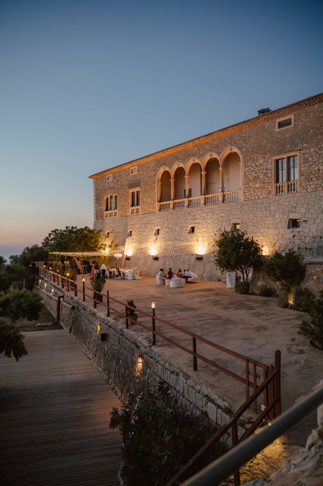 A Mediterranean stone villa illuminated at dusk with arched windows and outdoor lighting.