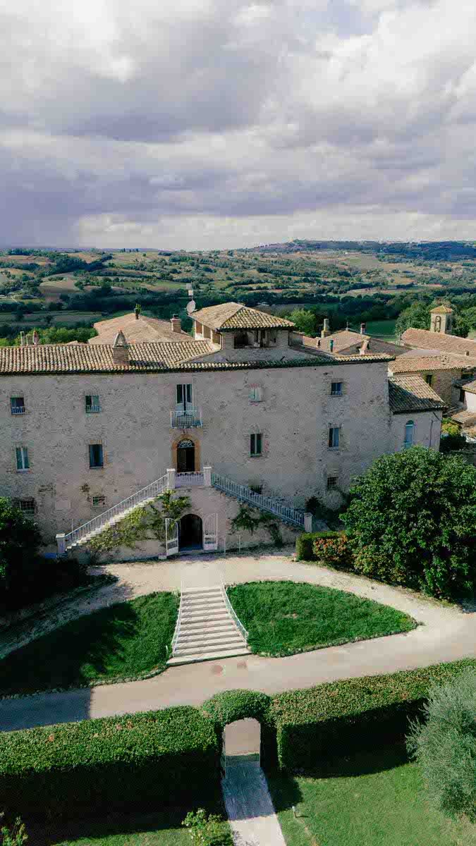 Aerial view of rustic Italian villa with stone architecture and manicured gardens.