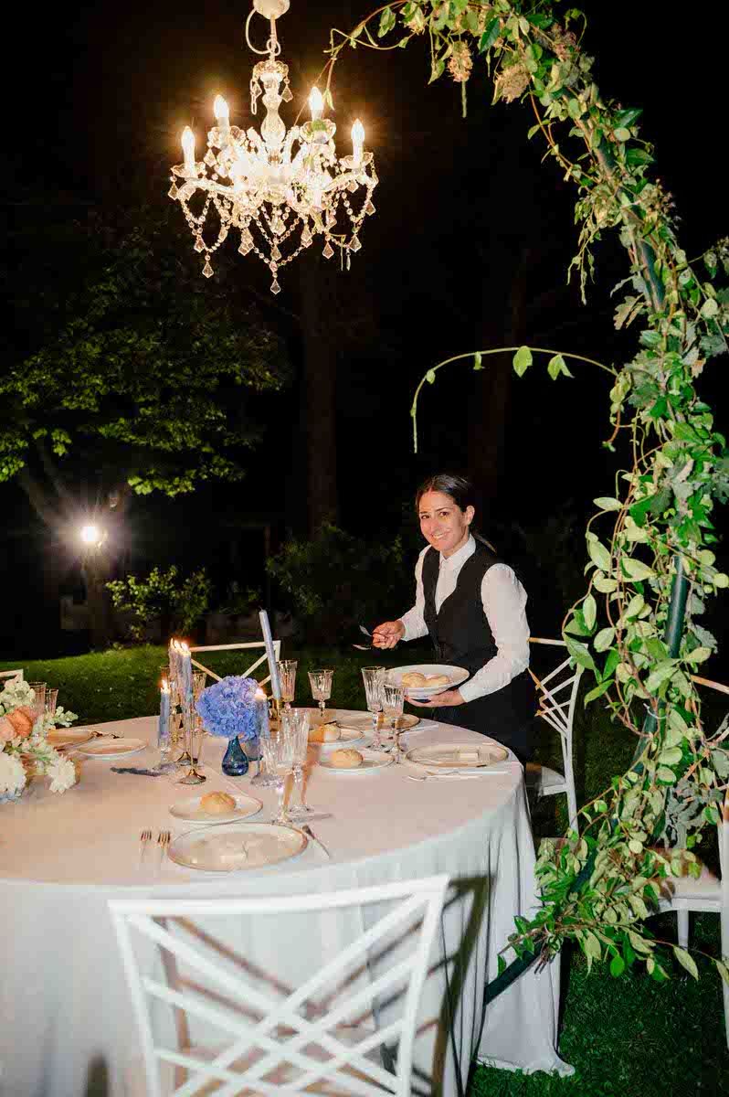 Table setting under crystal chandelier with ivy arch and evening ambiance.