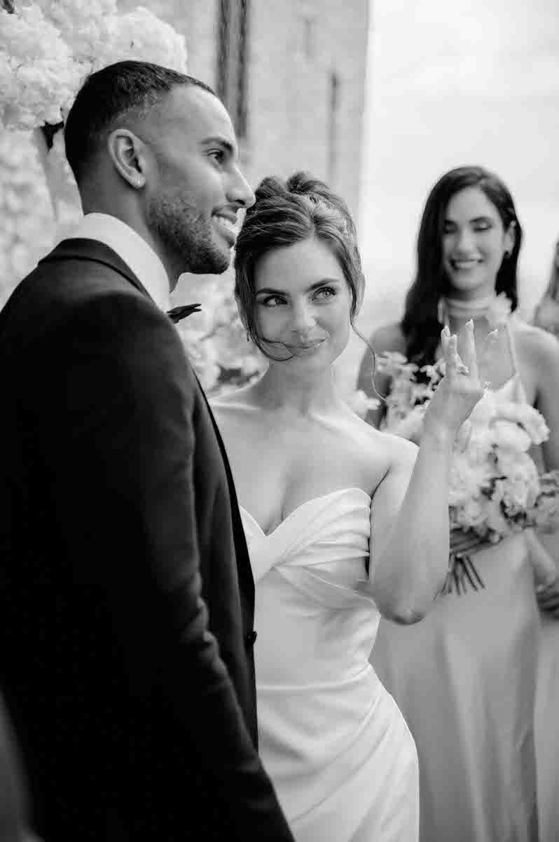 Elegant wedding moment captured in black and white at stone venue with attendant in background.