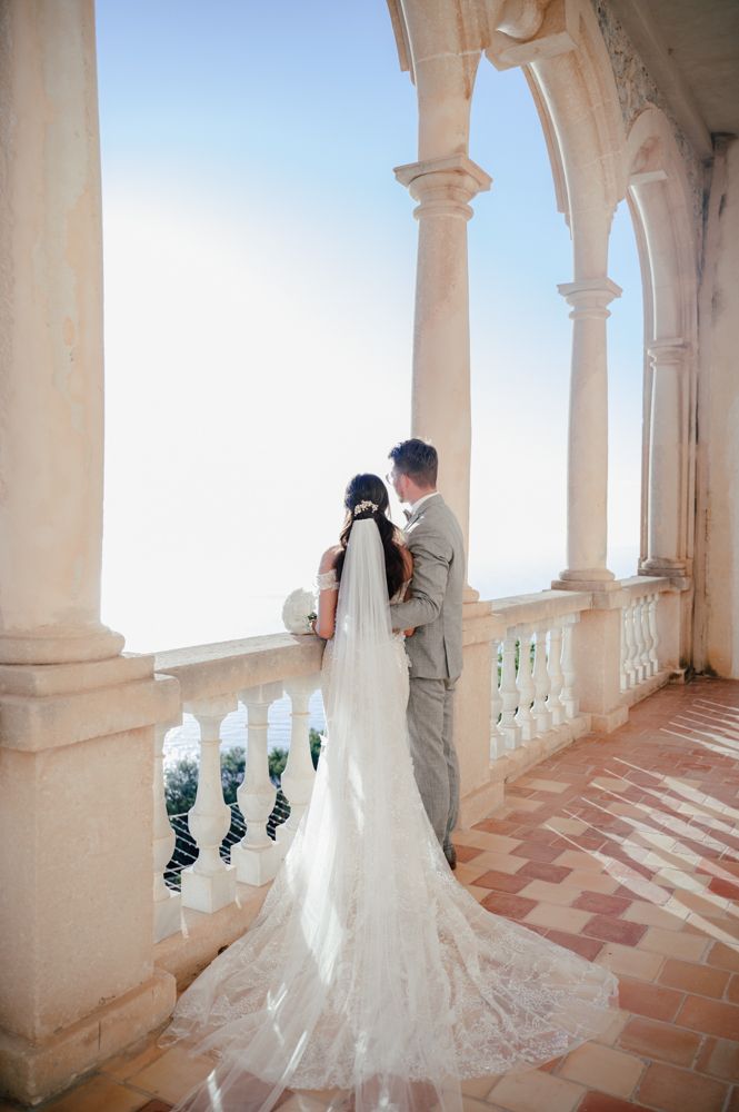 A couple admires the view from a columned terrace with a long flowing wedding veil.