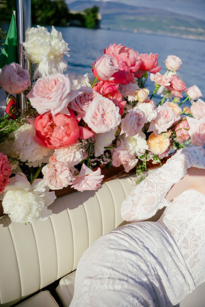Beautiful floral arrangement with pink and white roses and peonies in a cream-colored vessel against a scenic lake backdrop.