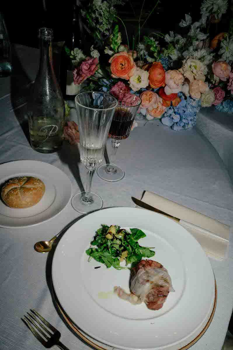 Plated dinner with colorful floral arrangements and wine glasses at elegant reception.