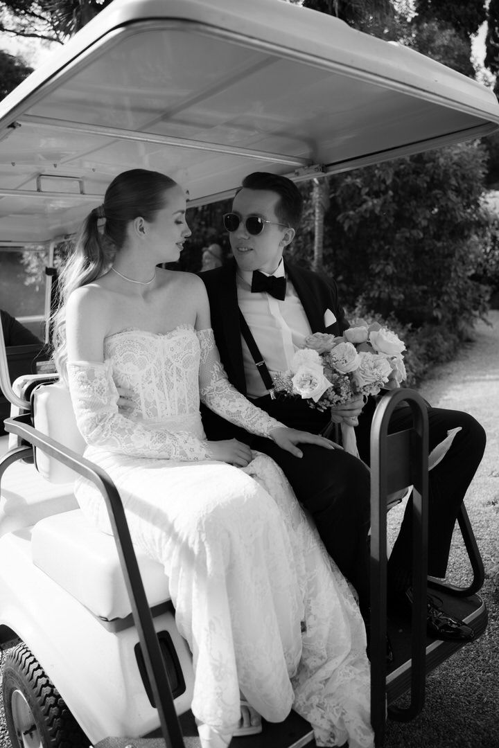 Bride in a white wedding gown being helped into a golf cart after a wedding ceremony.