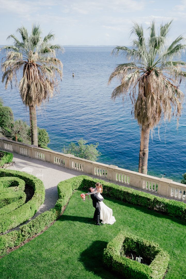 Aerial view of two palm trees and manicured garden overlooking a Mediterranean coastline with stone balustrade.