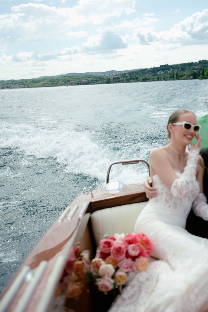 Elegant wedding scene on a boat with pink floral bouquet and lake view in the background.