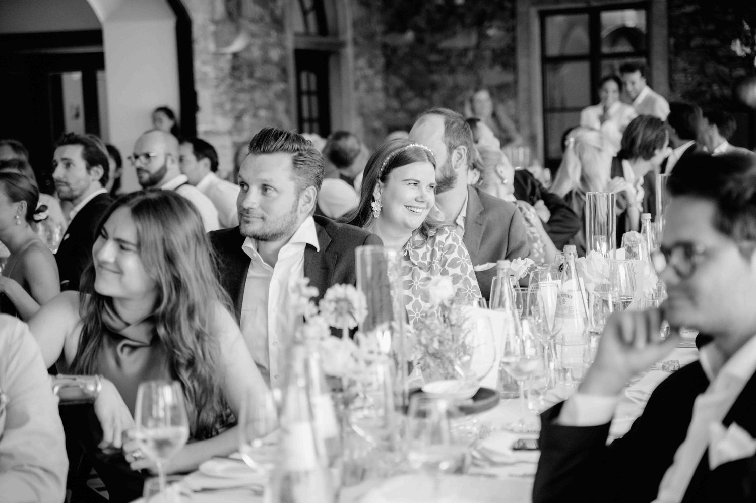 Panoramic black and white photo showing wedding guests seated at long tables during an elegant reception dinner.