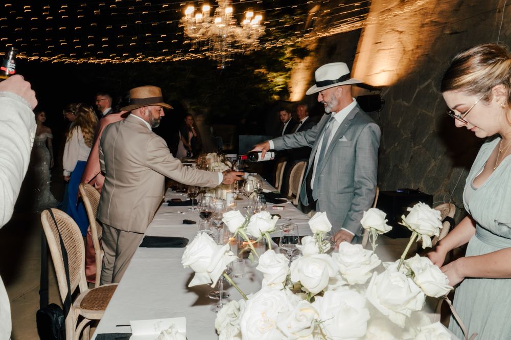Wedding guests serve dinner at an elegant reception with white floral centerpieces.