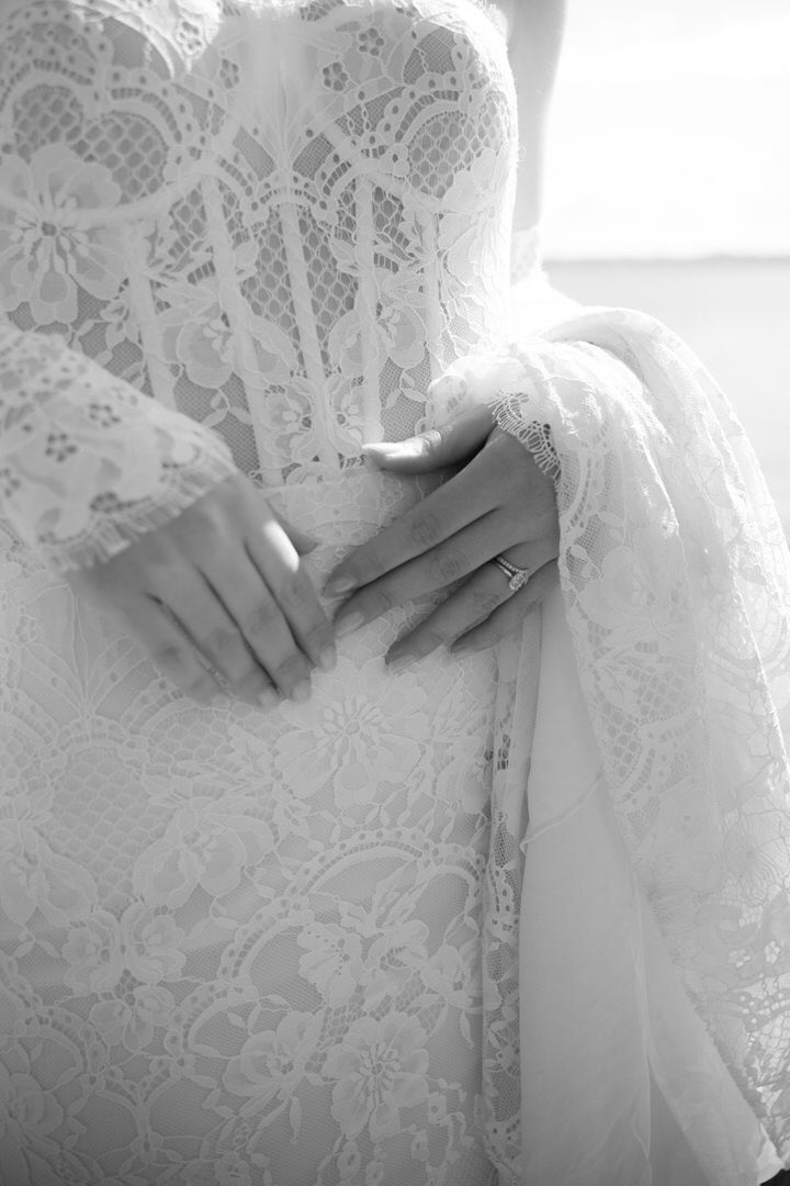 Close-up shot of delicate white lace wedding dress details with hands gently touching the intricate fabric pattern.