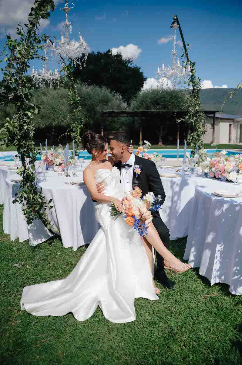 Newlyweds share intimate moment at outdoor reception with elegant white table settings.