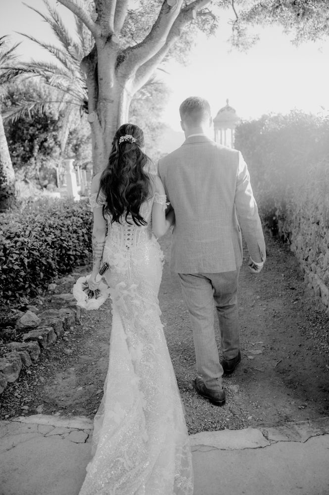 A black and white photo of a wedding couple walking along a garden path.