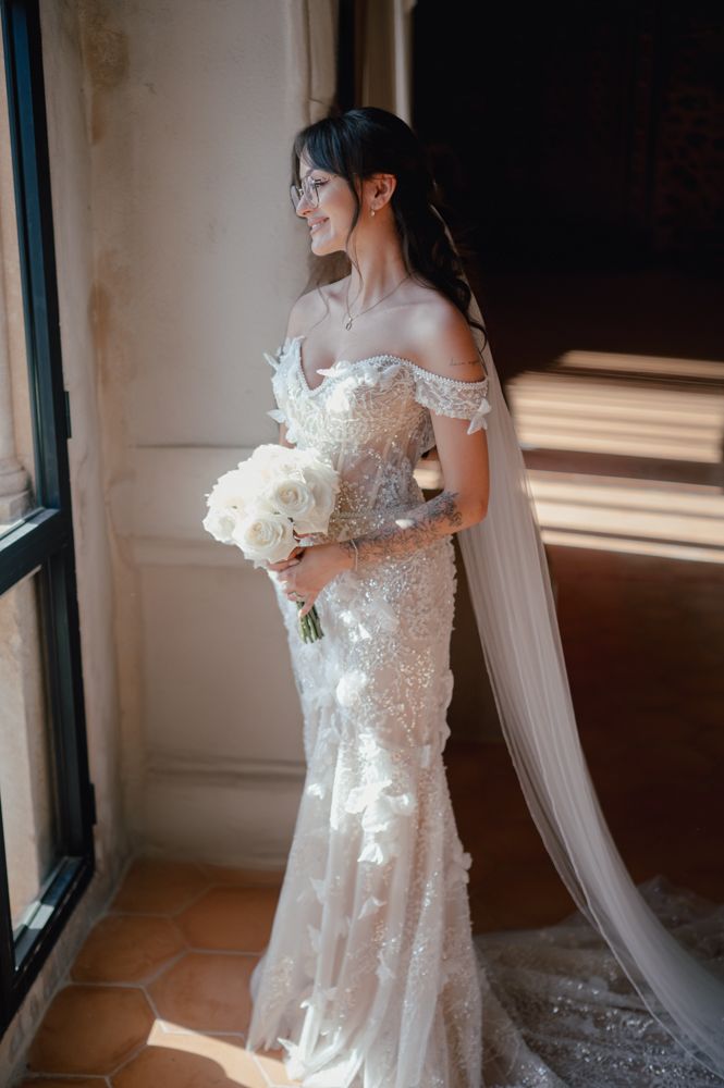 Bridal portrait featuring an off-shoulder lace wedding gown with flowing veil.