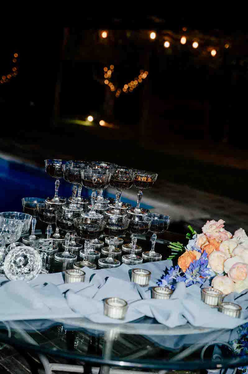 Champagne tower display with floral decorations and candles at night.