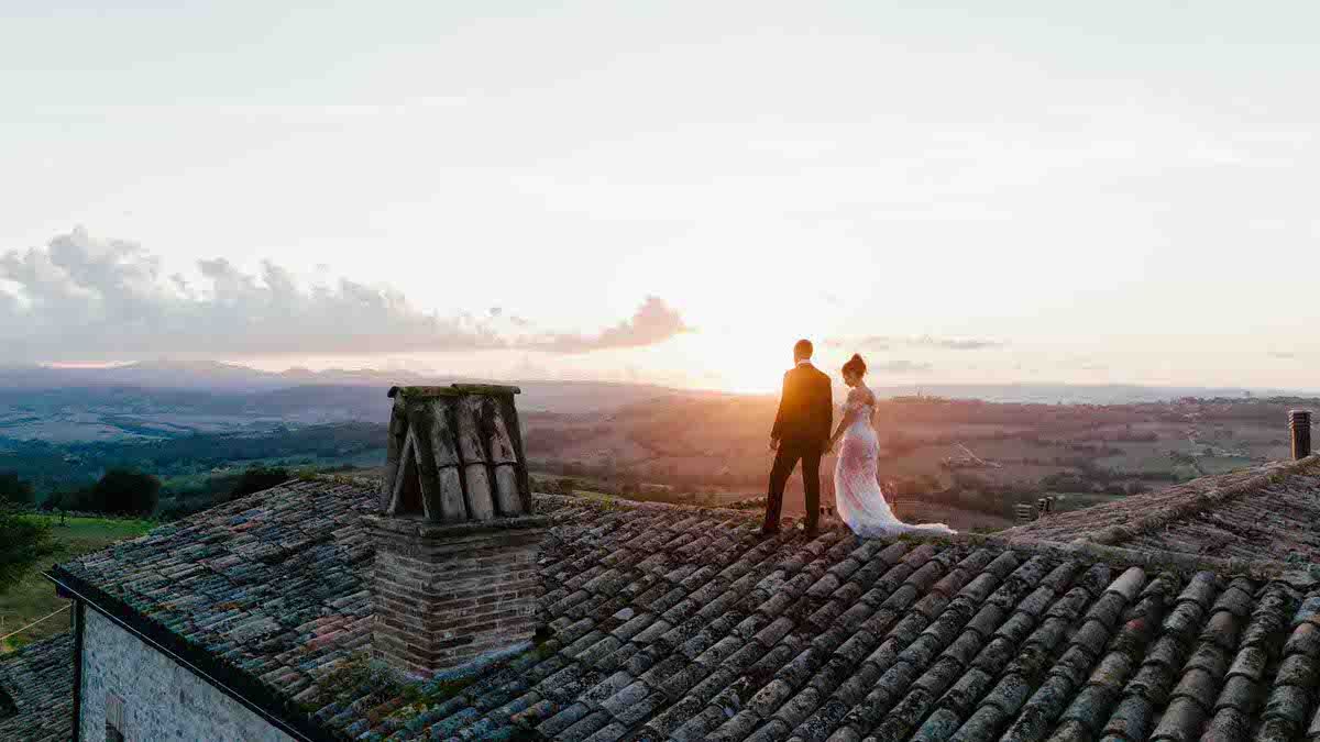 Wedding couple silhouetted against sunset sky on Mediterranean rooftop with mountain views.