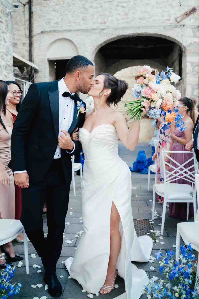 Romantic wedding moment at stone venue with elegant white dress and blue floral decorations.