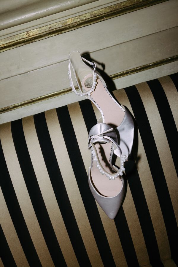 An elegant grey slingback heel shoe with a bow detail rests on a black and white striped surface.