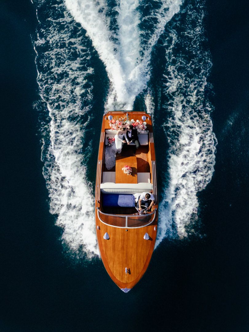 Aerial view of a wooden luxury speedboat creating dramatic wake patterns in dark blue ocean waters.