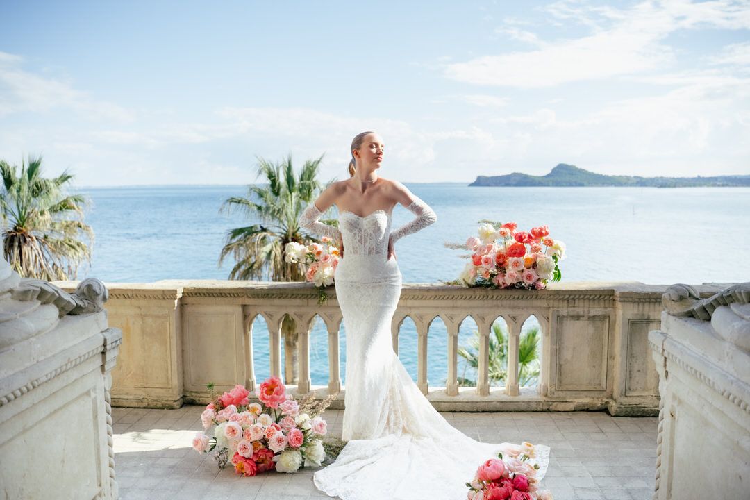 Scenic Mediterranean coastal wedding ceremony setup with white decor and coral floral arrangements on a seaside terrace.
