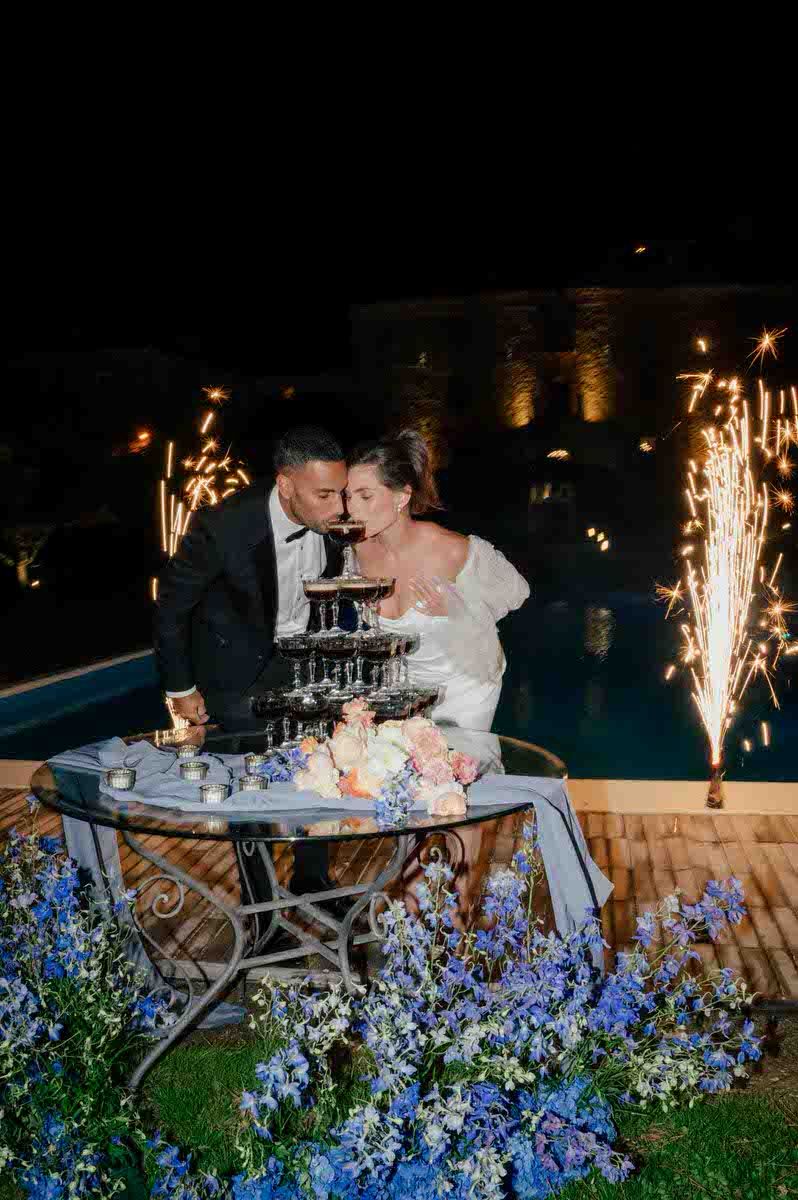 Wedding champagne tower with sparklers and blue flowers by poolside.