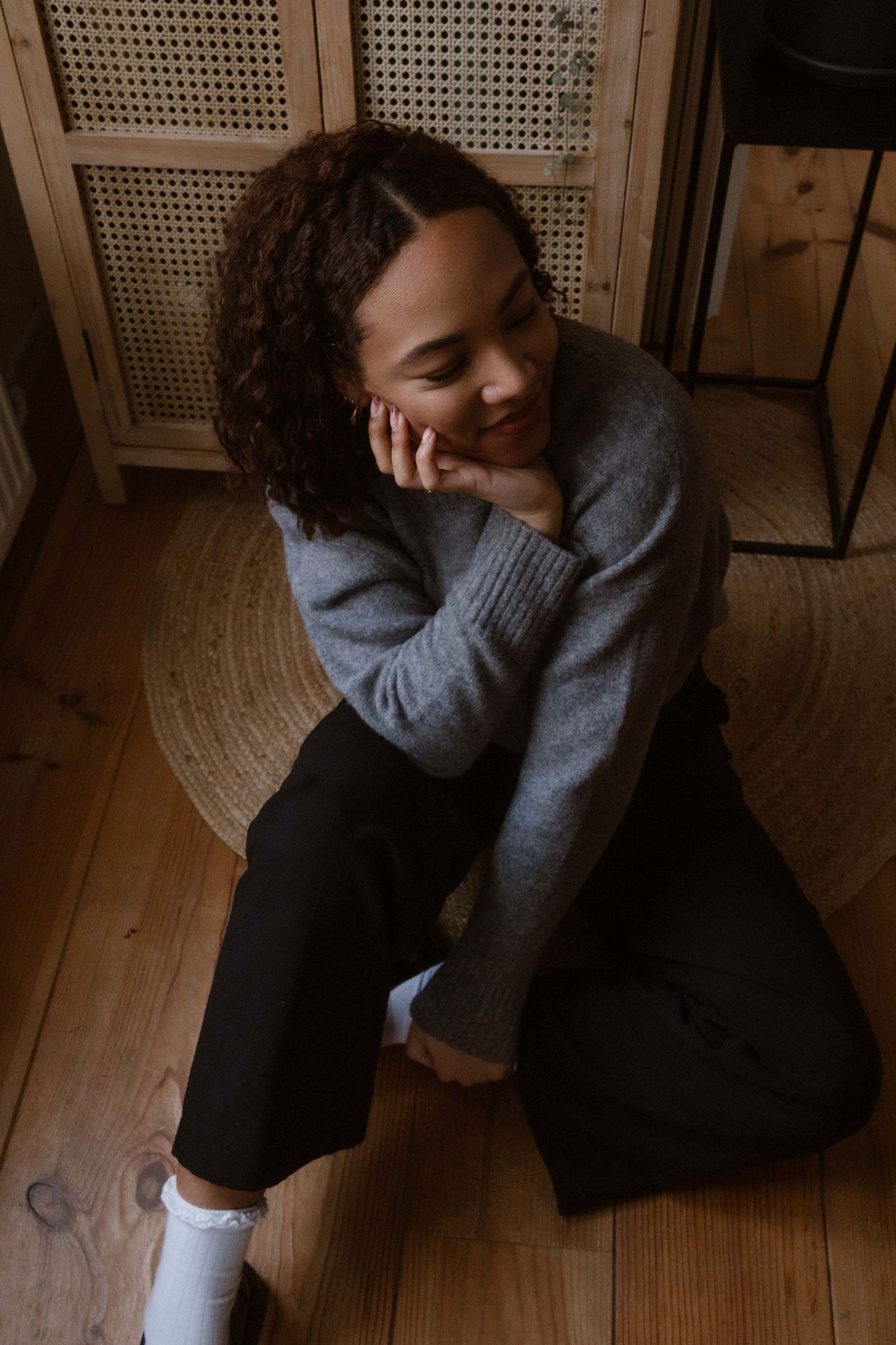 Person wearing a cozy gray sweater sits relaxed on wooden floor with natural lighting.