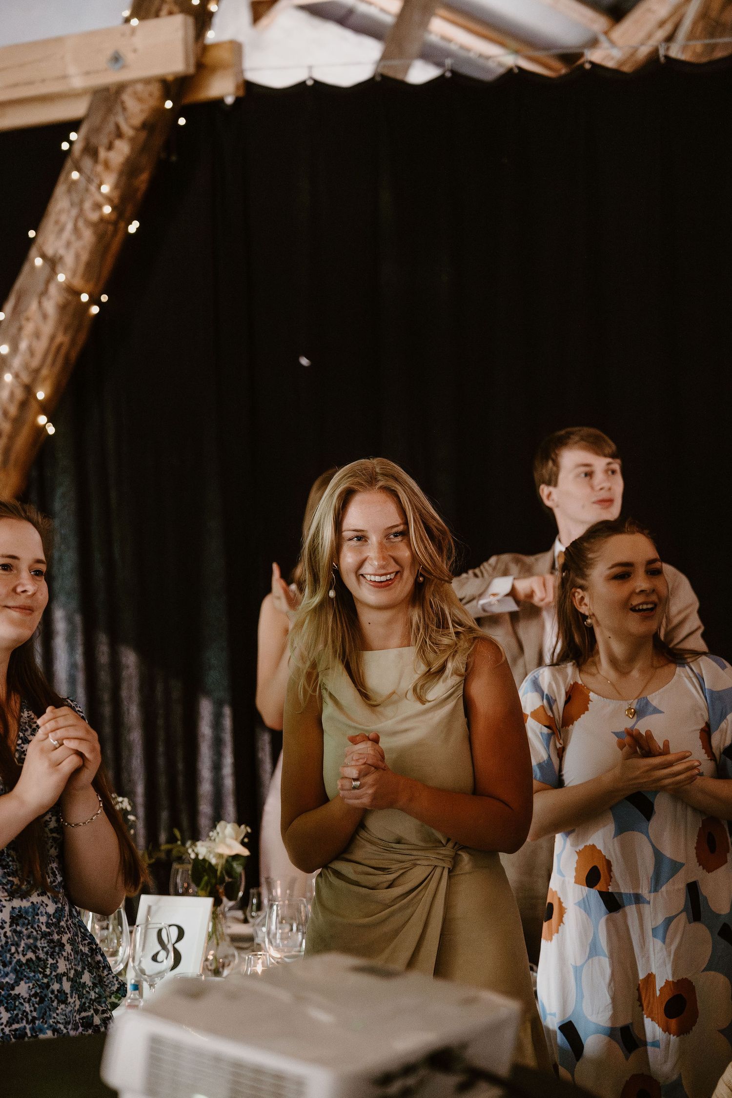 Group of wedding guests dancing and celebrating at a reception with festive lighting and decor.