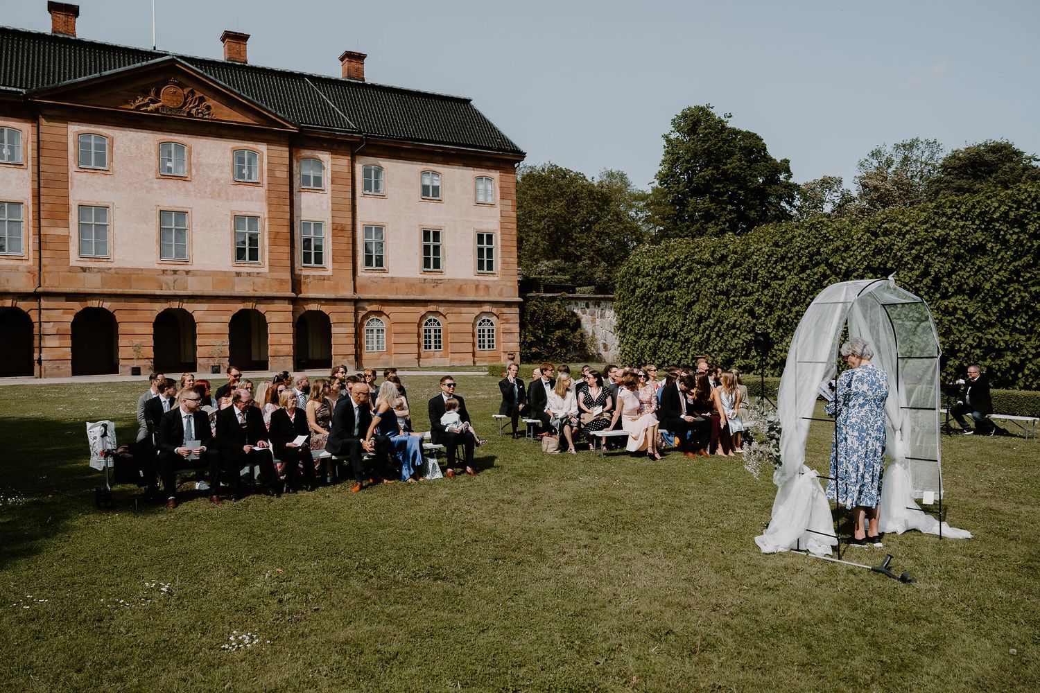 An elegant wedding ceremony setup at a historic manor with guests gathered on a sunny lawn for the outdoor celebration.