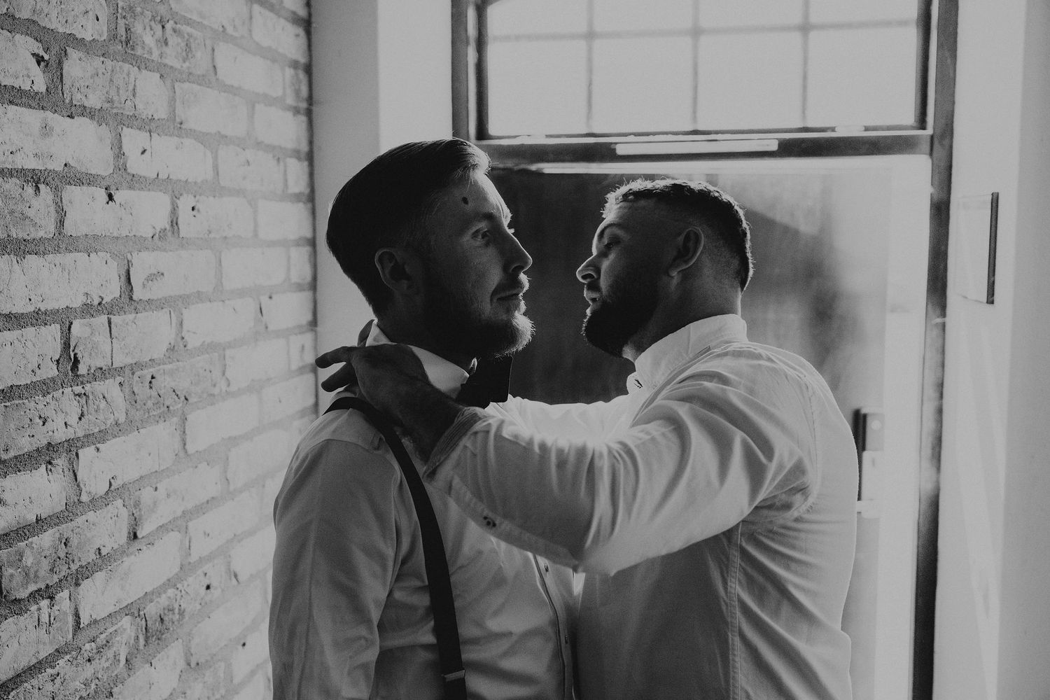 Black and white photo of two people in dress shirts having an emotional confrontation against a brick wall.