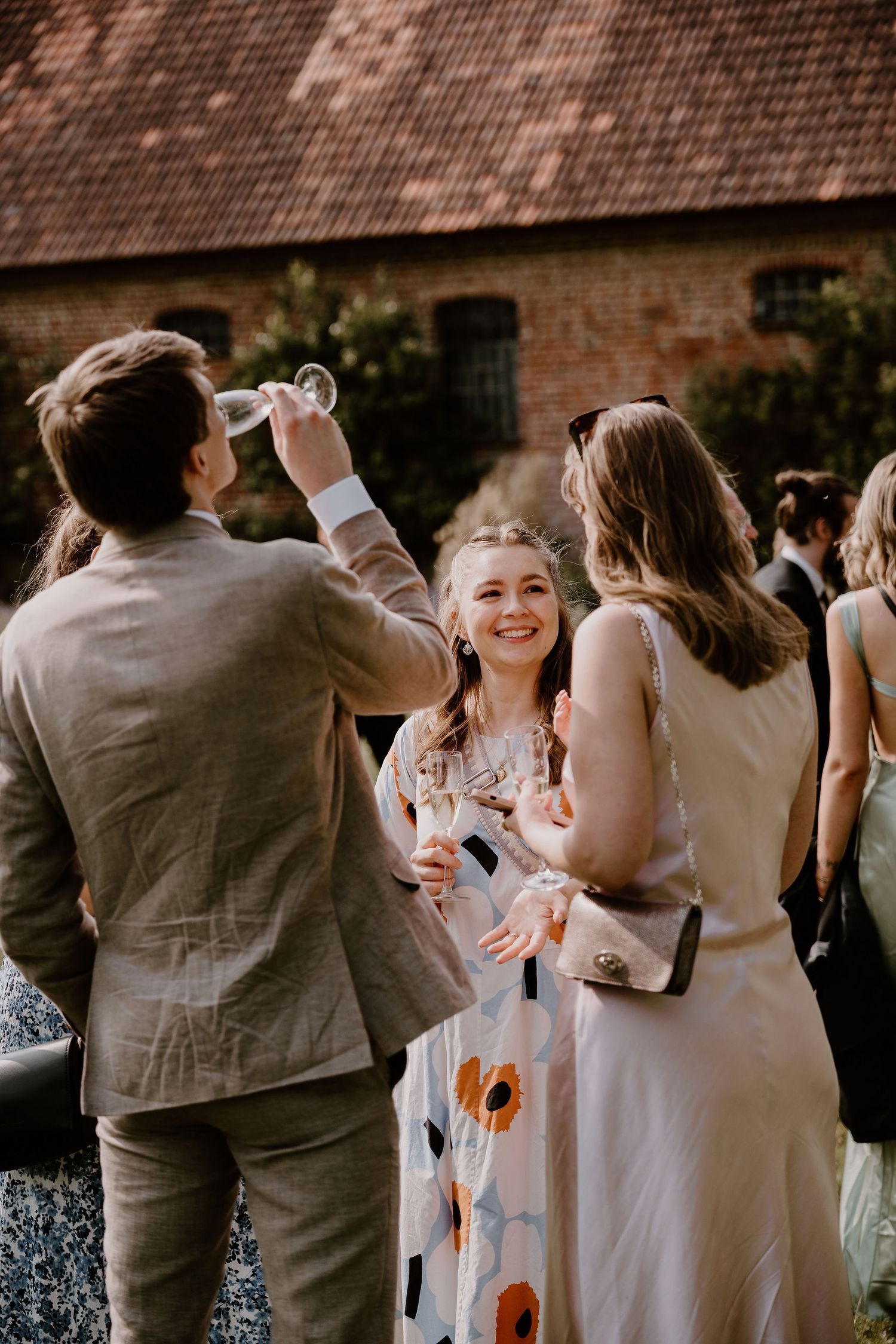 Wedding guests celebrate with couples dancing and mingling at an outdoor reception near a brick wall.