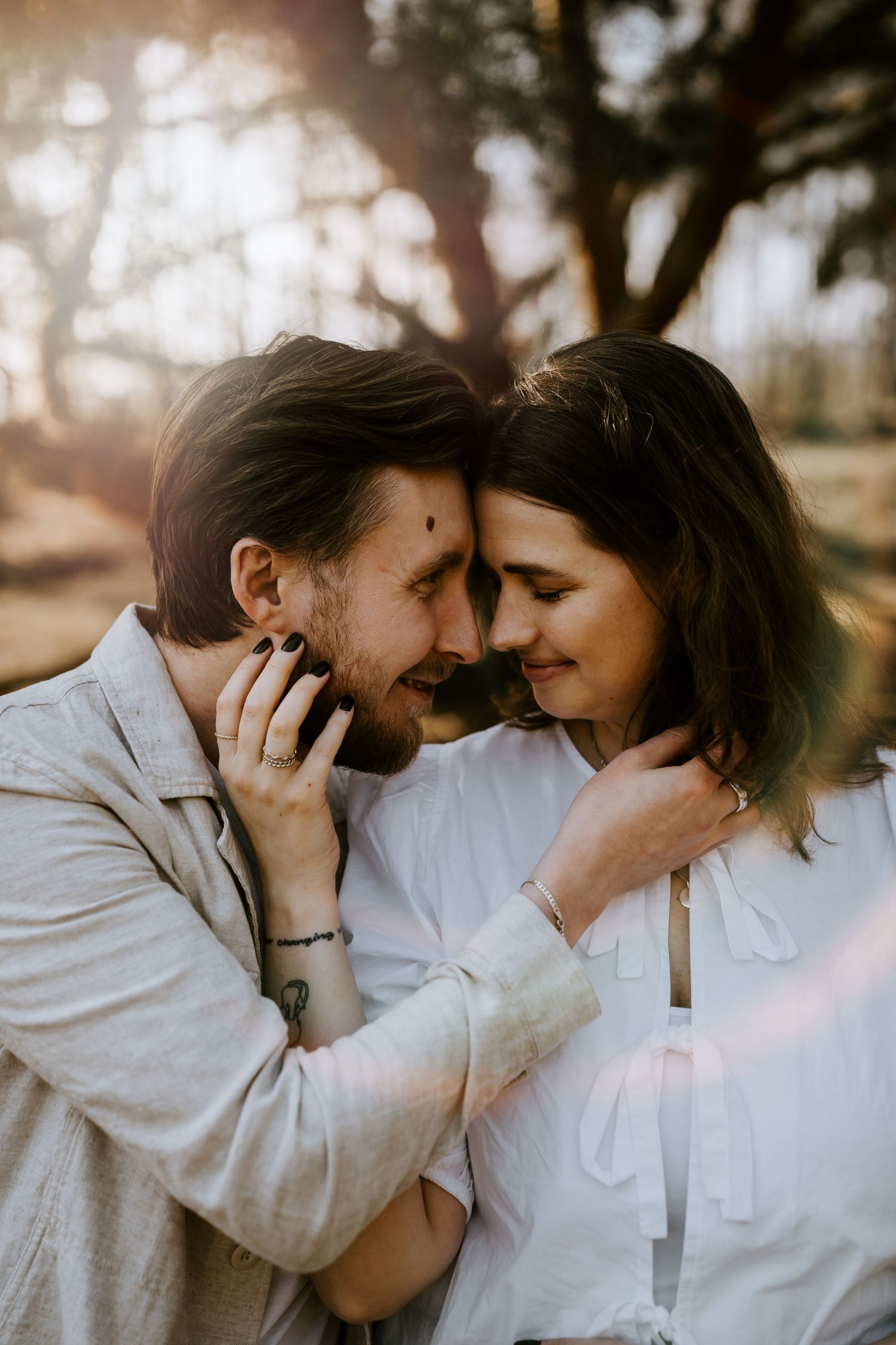 Romantic couple sharing an intimate moment outdoors at sunset with soft bokeh lighting through trees.