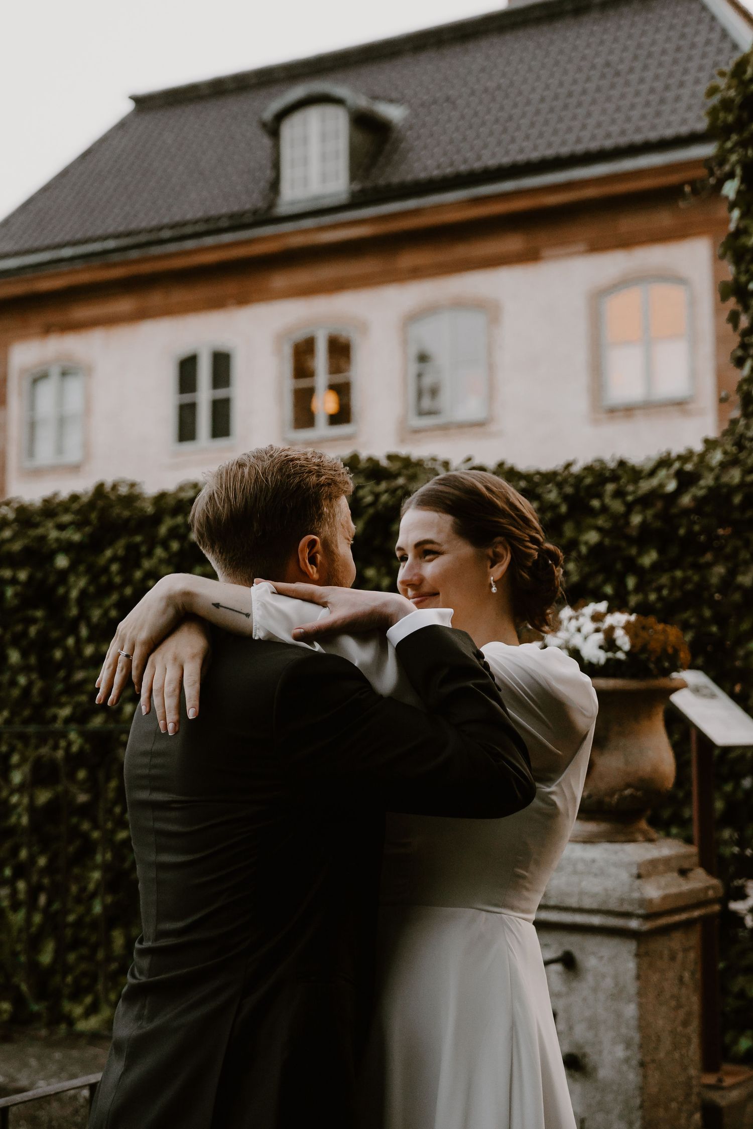 Two newlyweds sharing an intimate moment together in front of a vintage building exterior with ivy-covered walls.