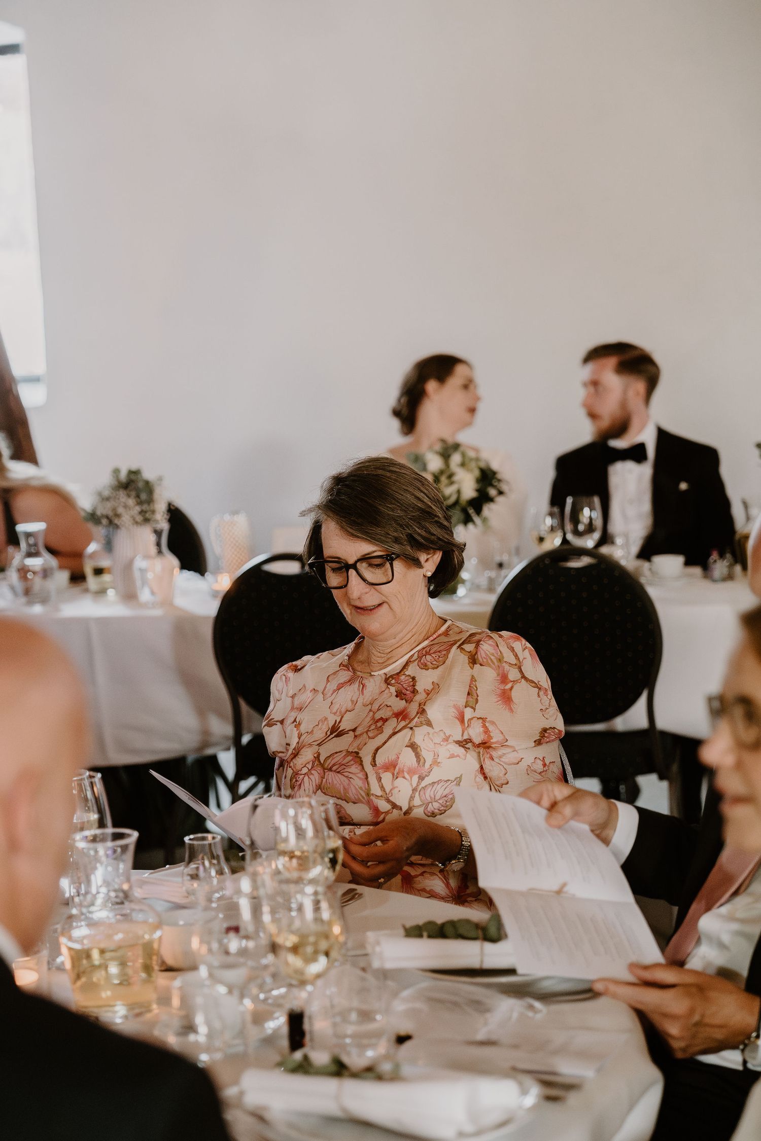 Wedding reception guests gathered at elegant tables with glassware and white linens for an intimate indoor celebration.