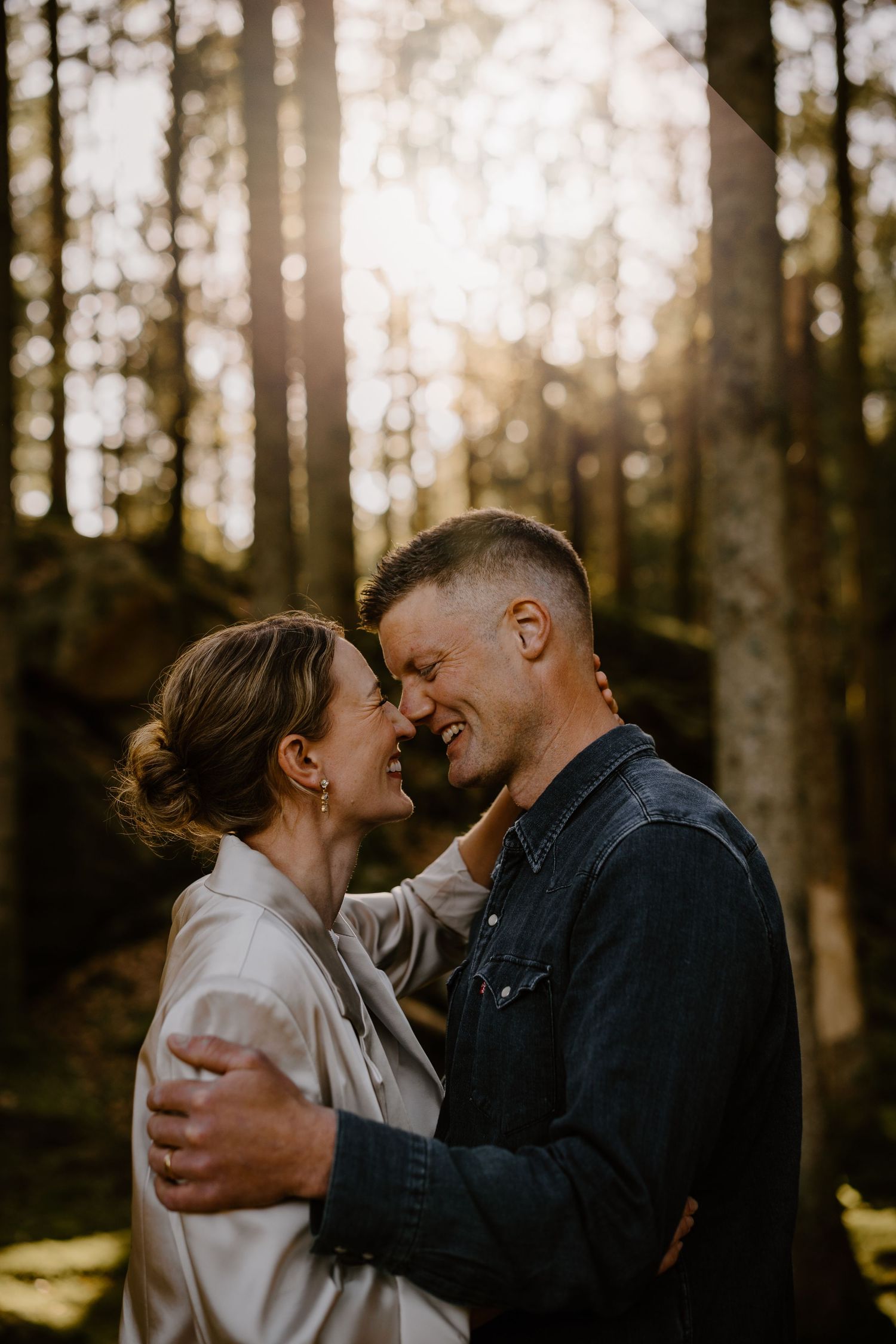 Intimate romantic moment between couple embracing in sunlit forest during golden hour.