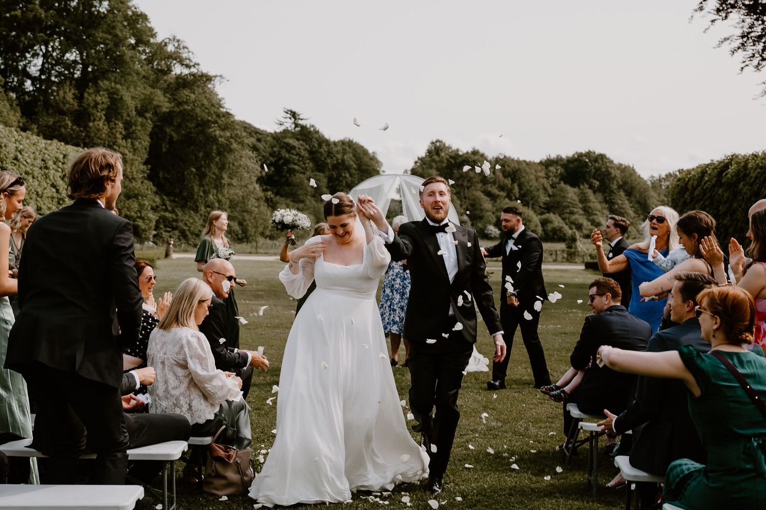 Wedding guests mingle and celebrate during an outdoor garden reception on a sunny afternoon.