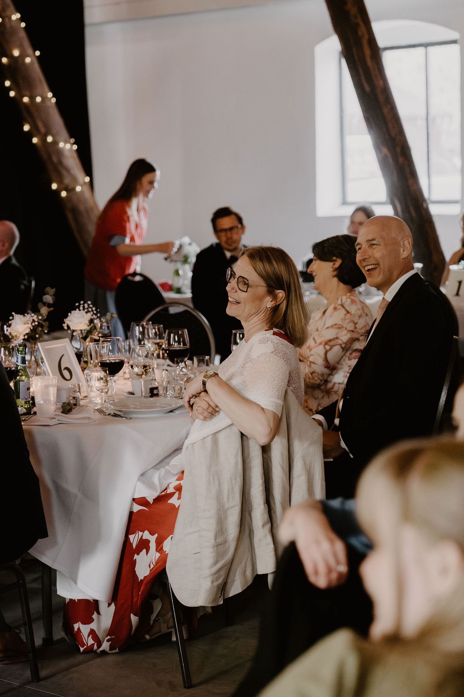 Guests laugh and enjoy themselves during an elegant dinner reception with sparkling string lights and white tablecloths.