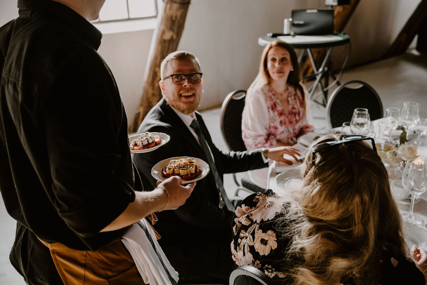 Guests enjoying bowls of food at a casual indoor gathering with natural lighting through windows.