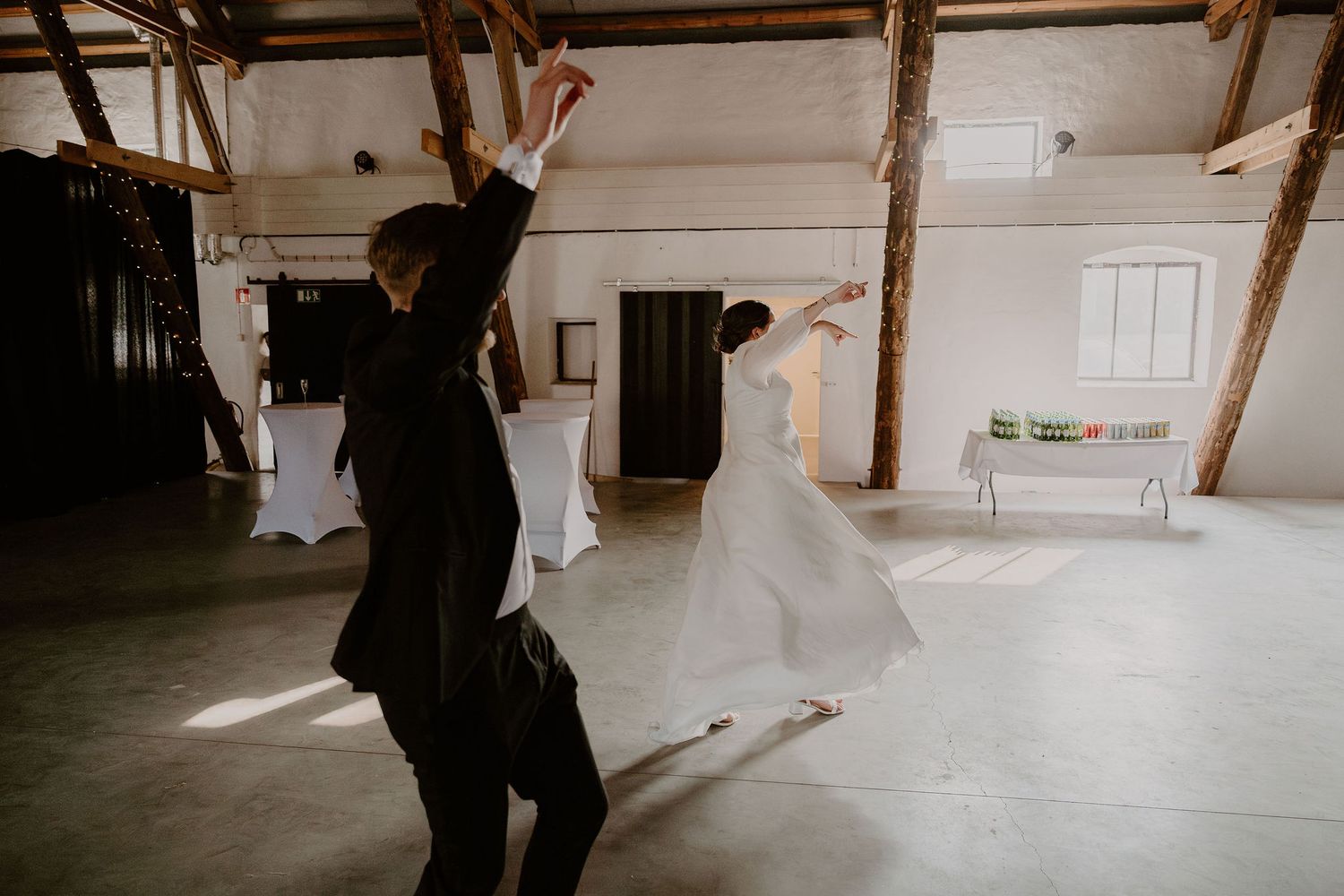 Two people dancing joyfully in an industrial style room with wooden beams and white walls.