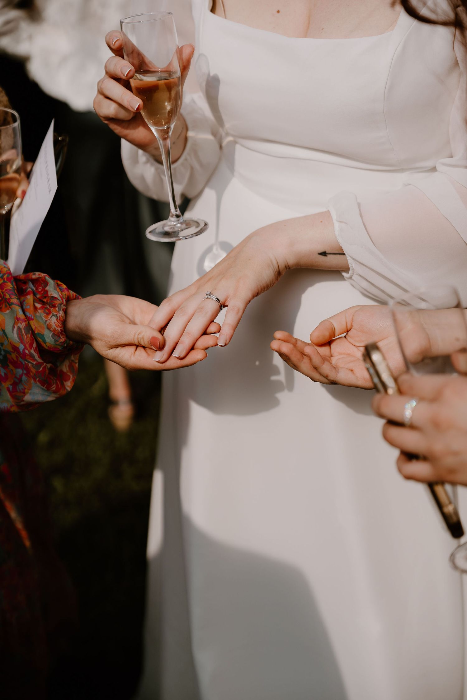Close-up of guests holding champagne glasses while looking at bride's engagement ring at wedding celebration.