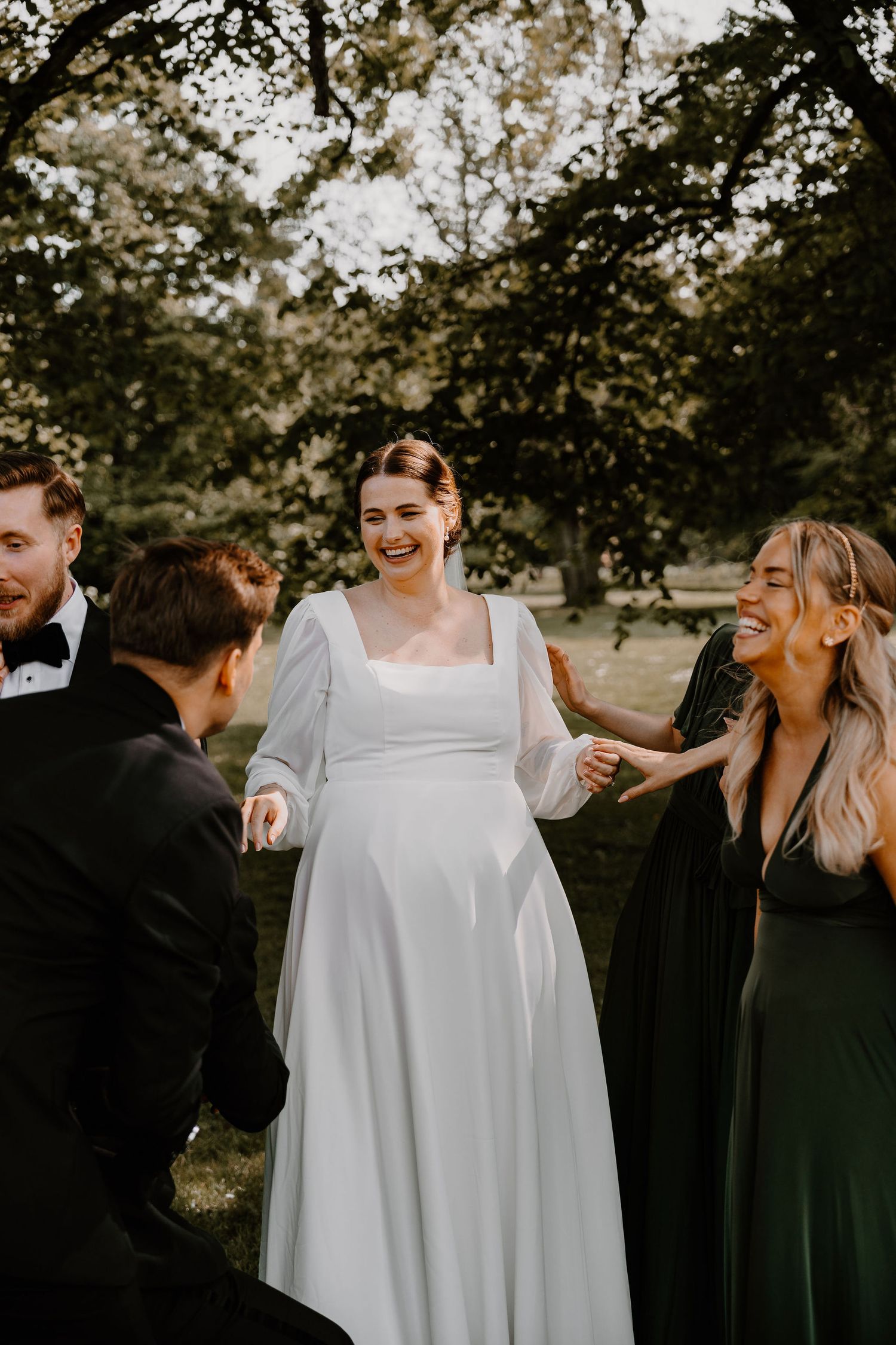 A bride in a white A-line gown shares a joyful moment with wedding guests outdoors during golden hour.