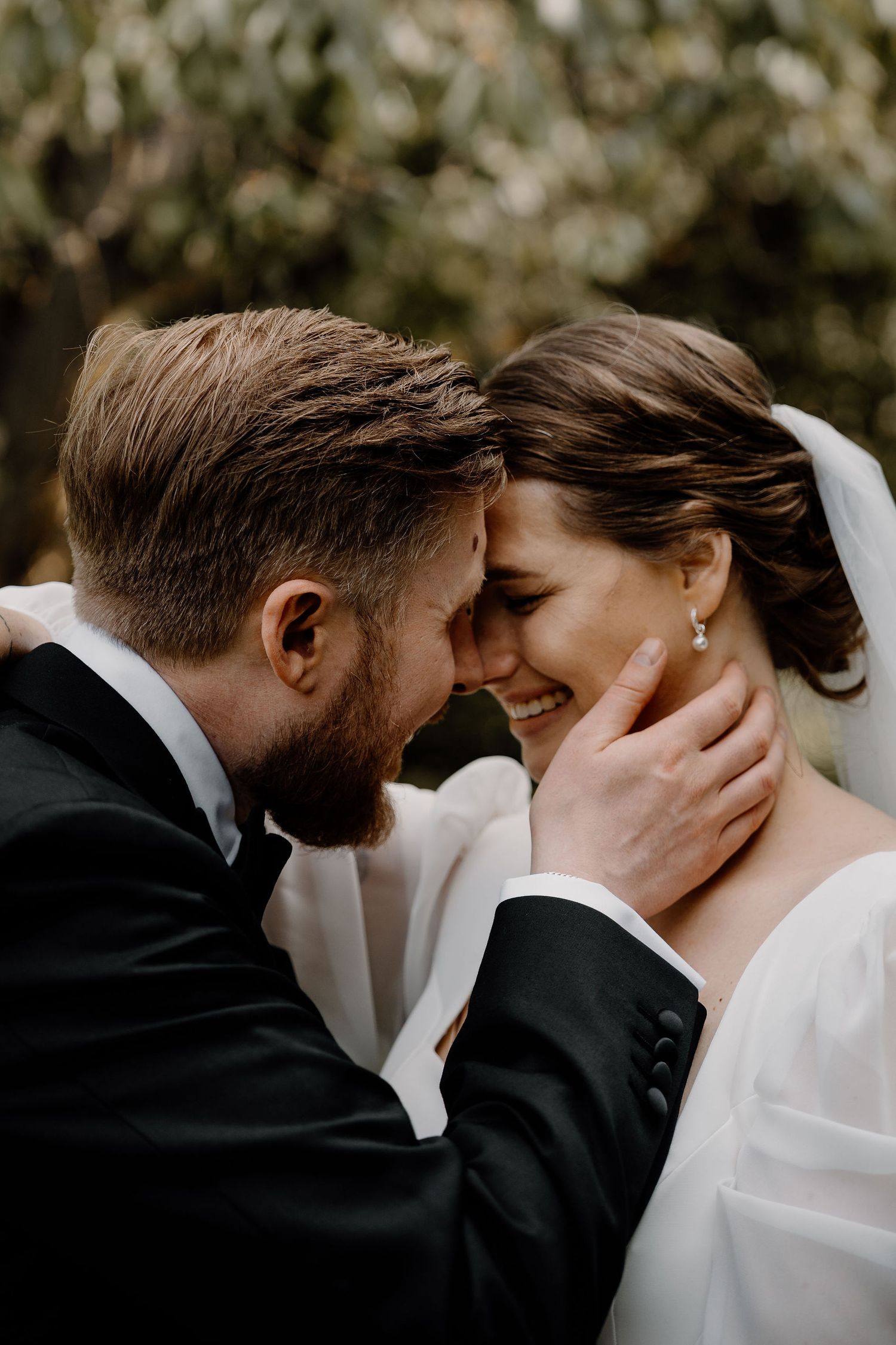Intimate wedding portrait of newlyweds sharing a tender moment against a soft, blurred natural background.