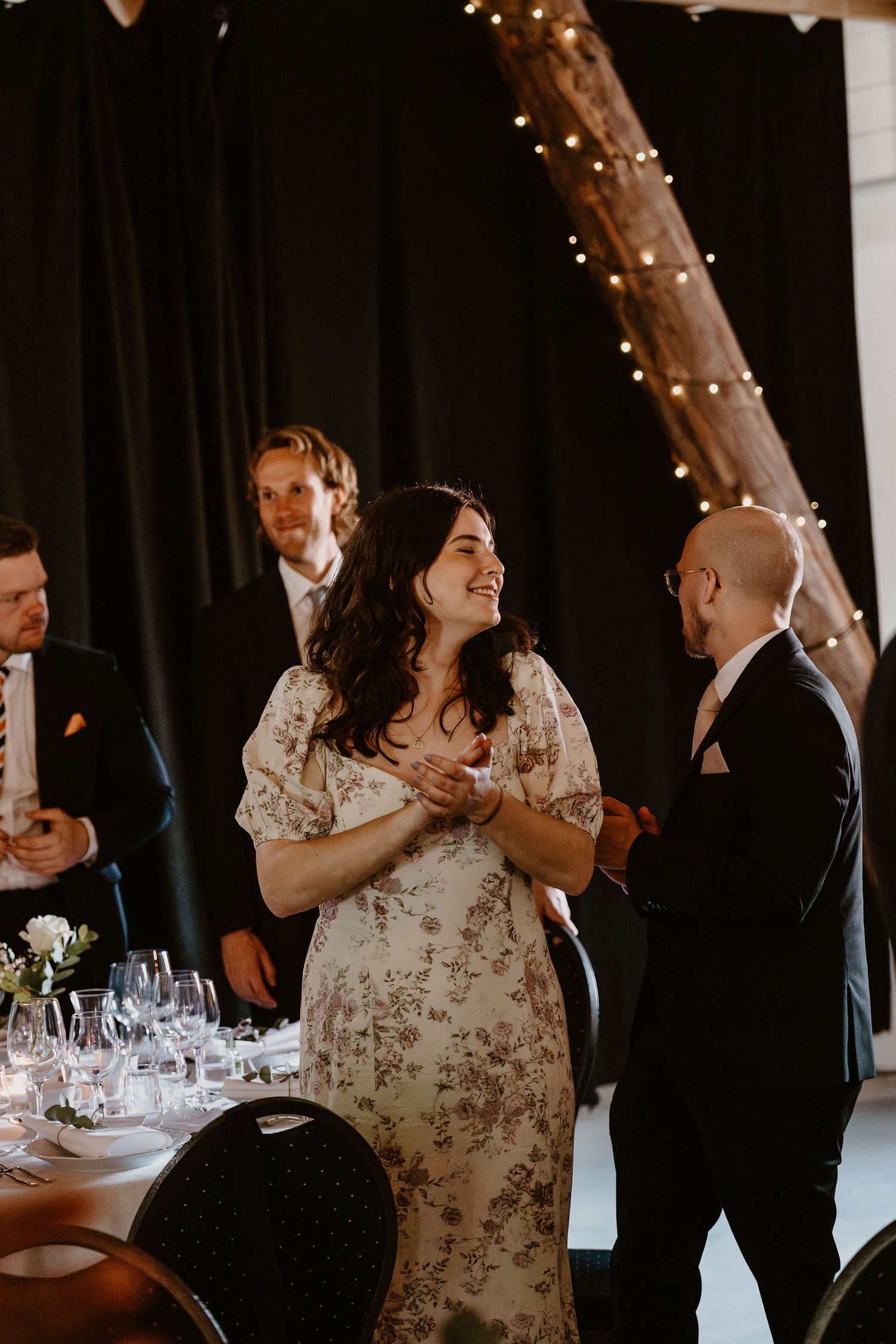 A romantic indoor wedding reception features decorative string lights, elegant table settings, and guests in formal attire.