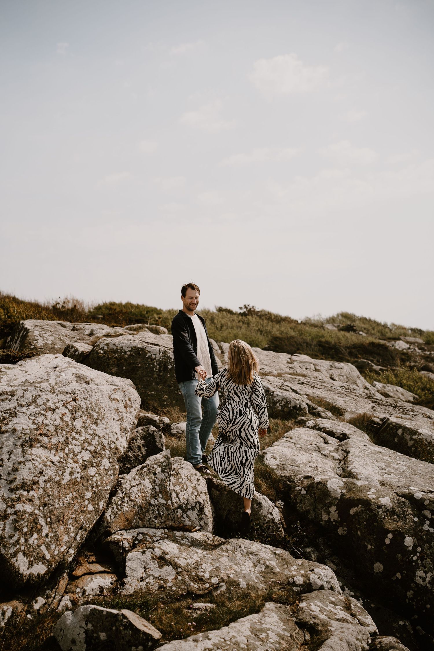 Two people standing together on rocky terrain against an overcast sky during an outdoor photo session.