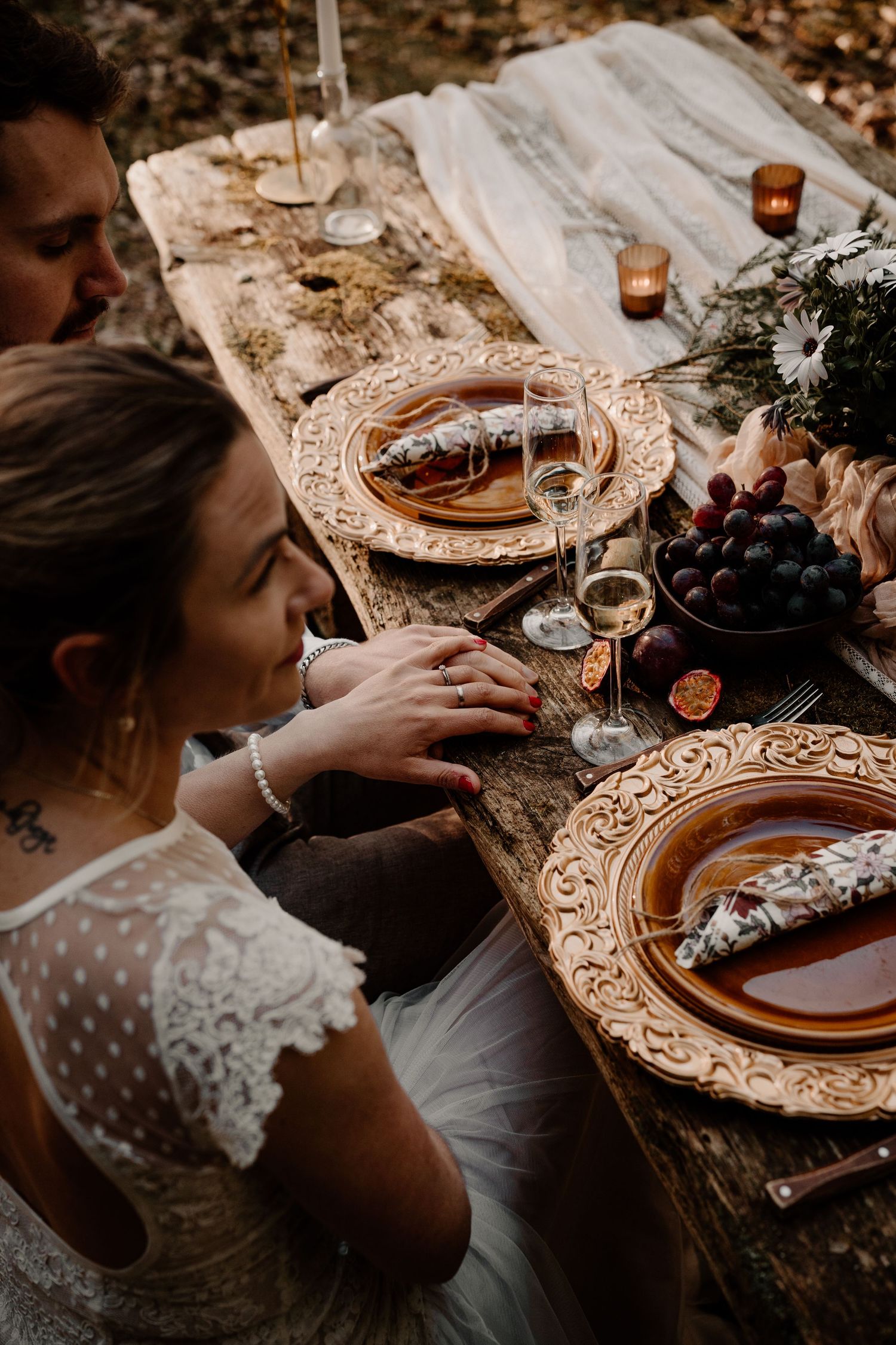 Elegant place settings with ornate gold charger plates and white lace details at a romantic outdoor dining setup.