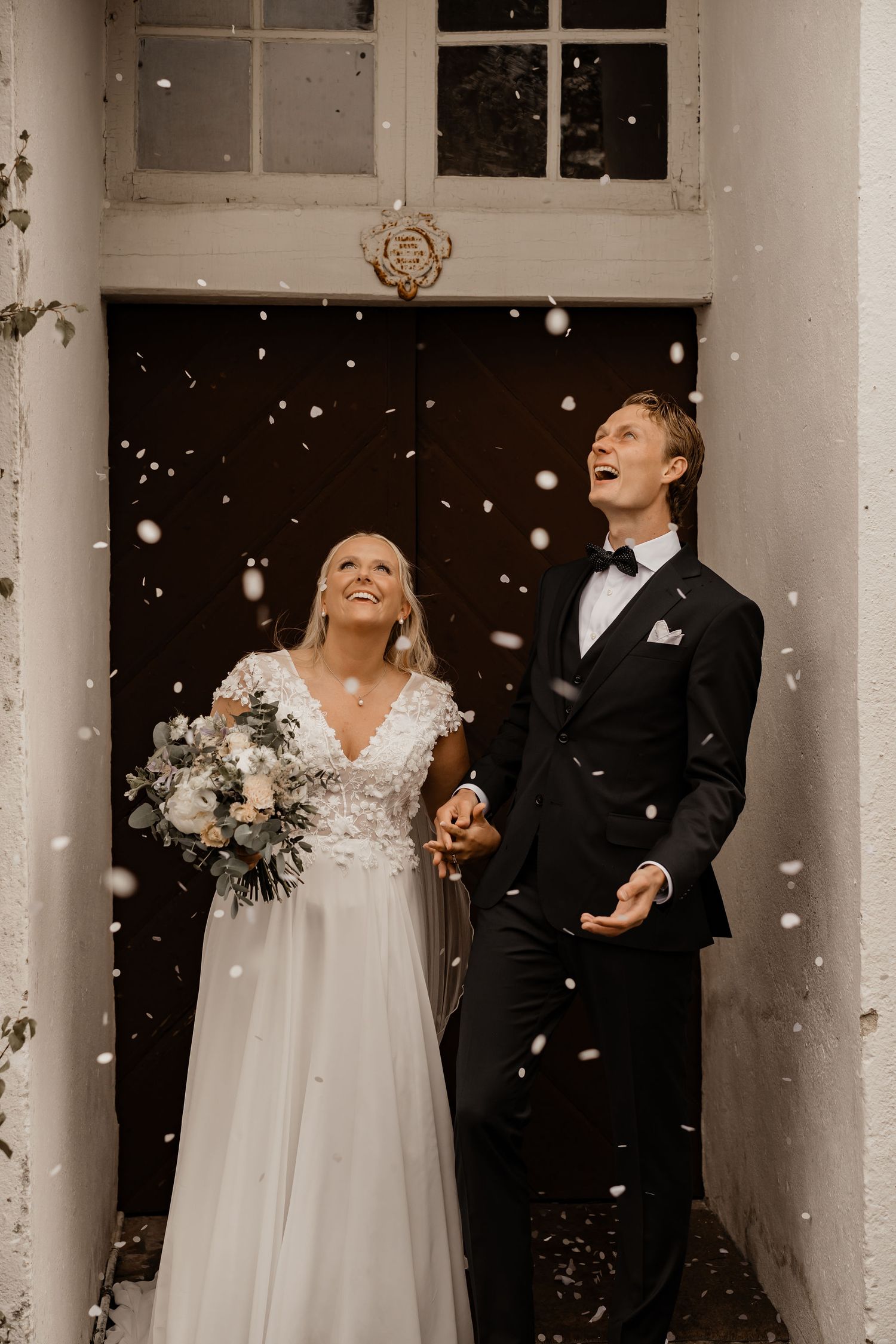 A joyful wedding couple laughs together as snow falls around them in a romantic outdoor winter scene.
