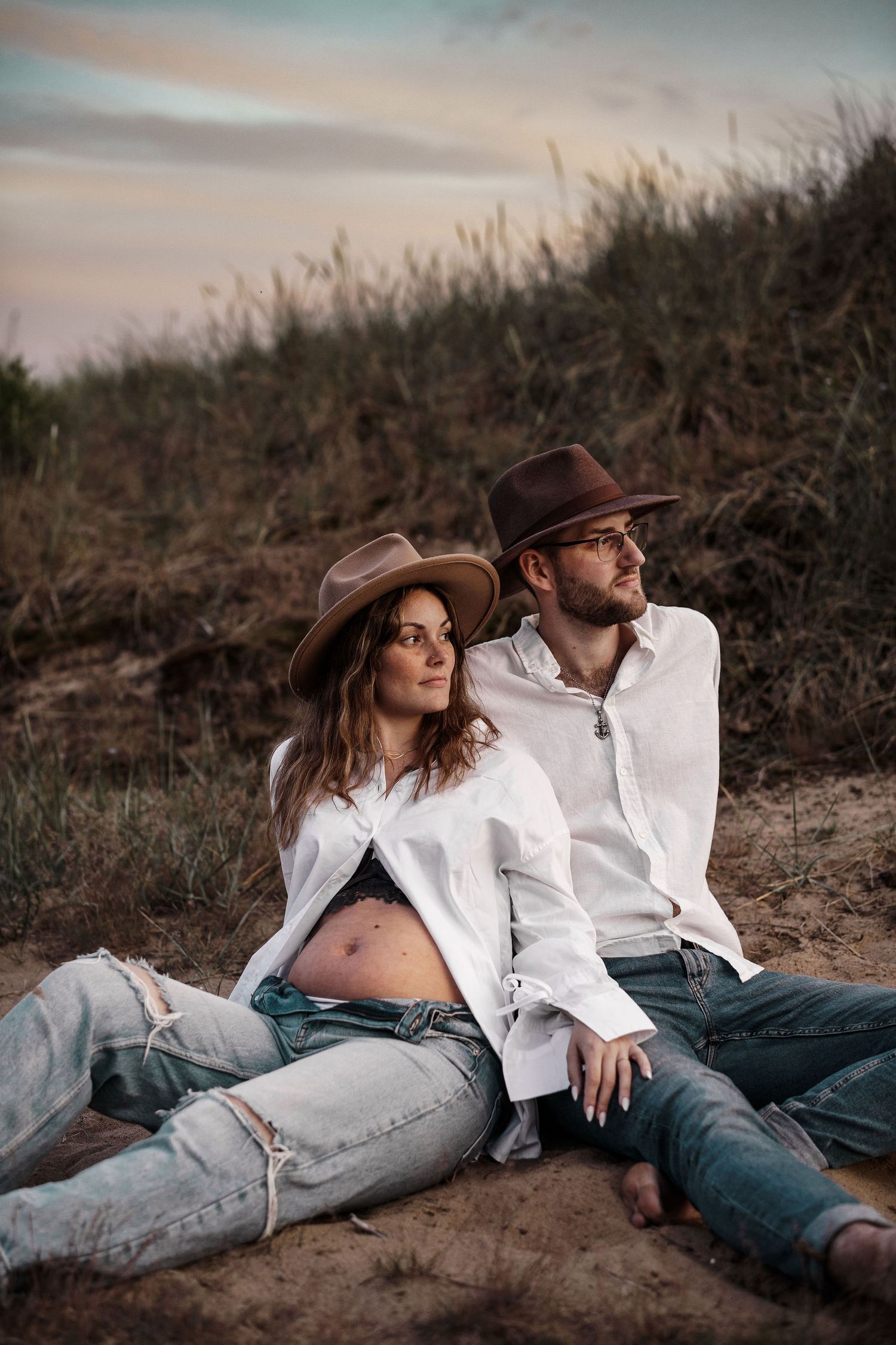 Couple in white shirts and cowboy hats pose for romantic sunset maternity photos.