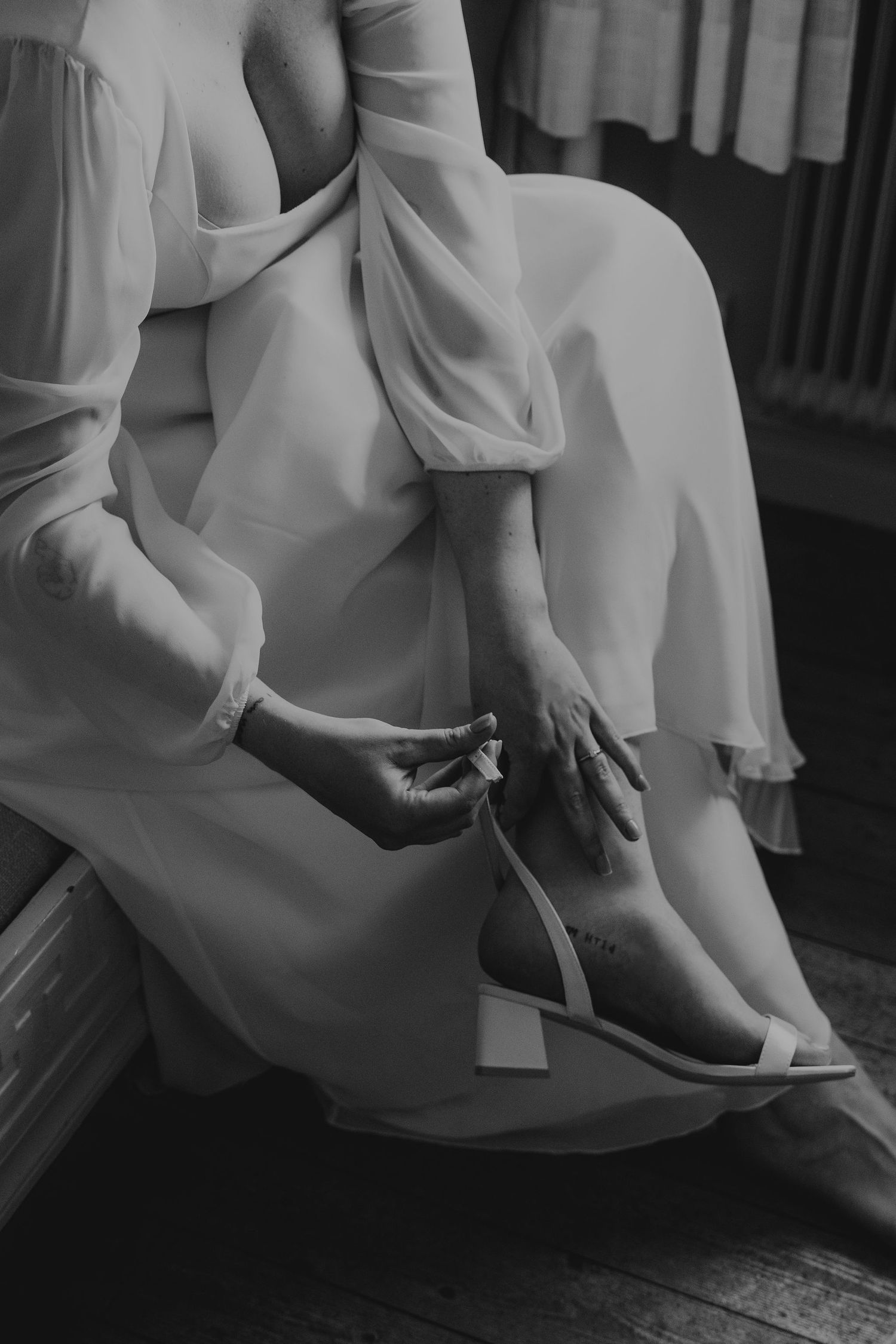 Close-up black and white shot of a bride fastening her elegant white wedding shoes.