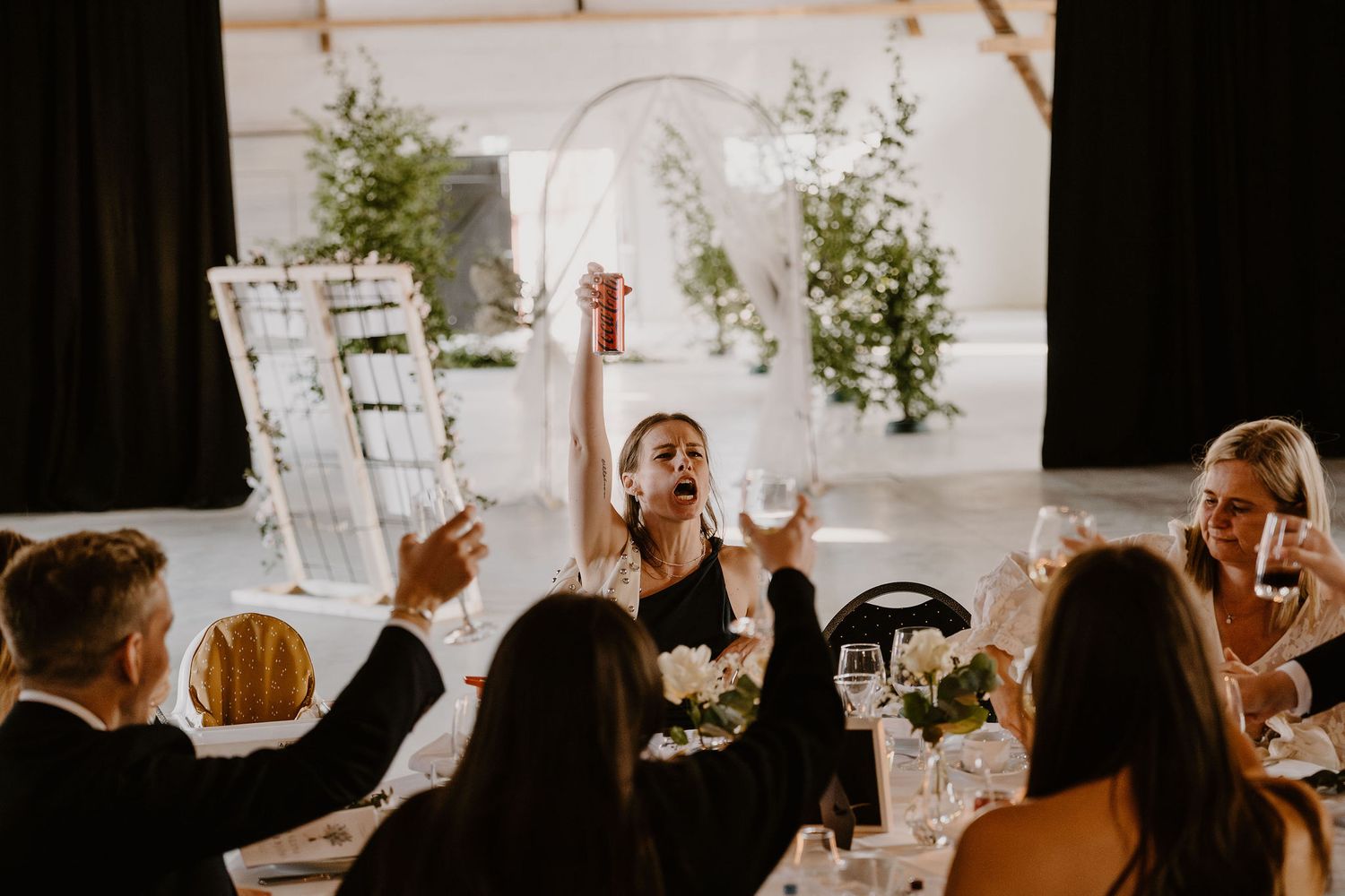 Elegant wedding reception table setting with greenery, florals, and candlelight as guests celebrate in warm glowing light.