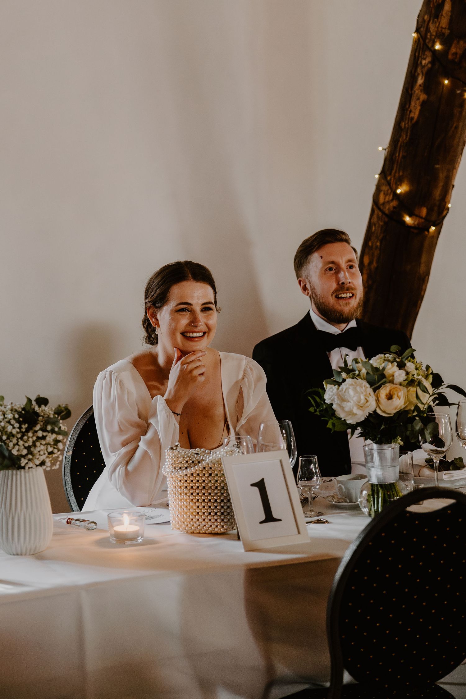Newlyweds share a happy moment together at their wedding reception table decorated with floral centerpieces and candlelight.