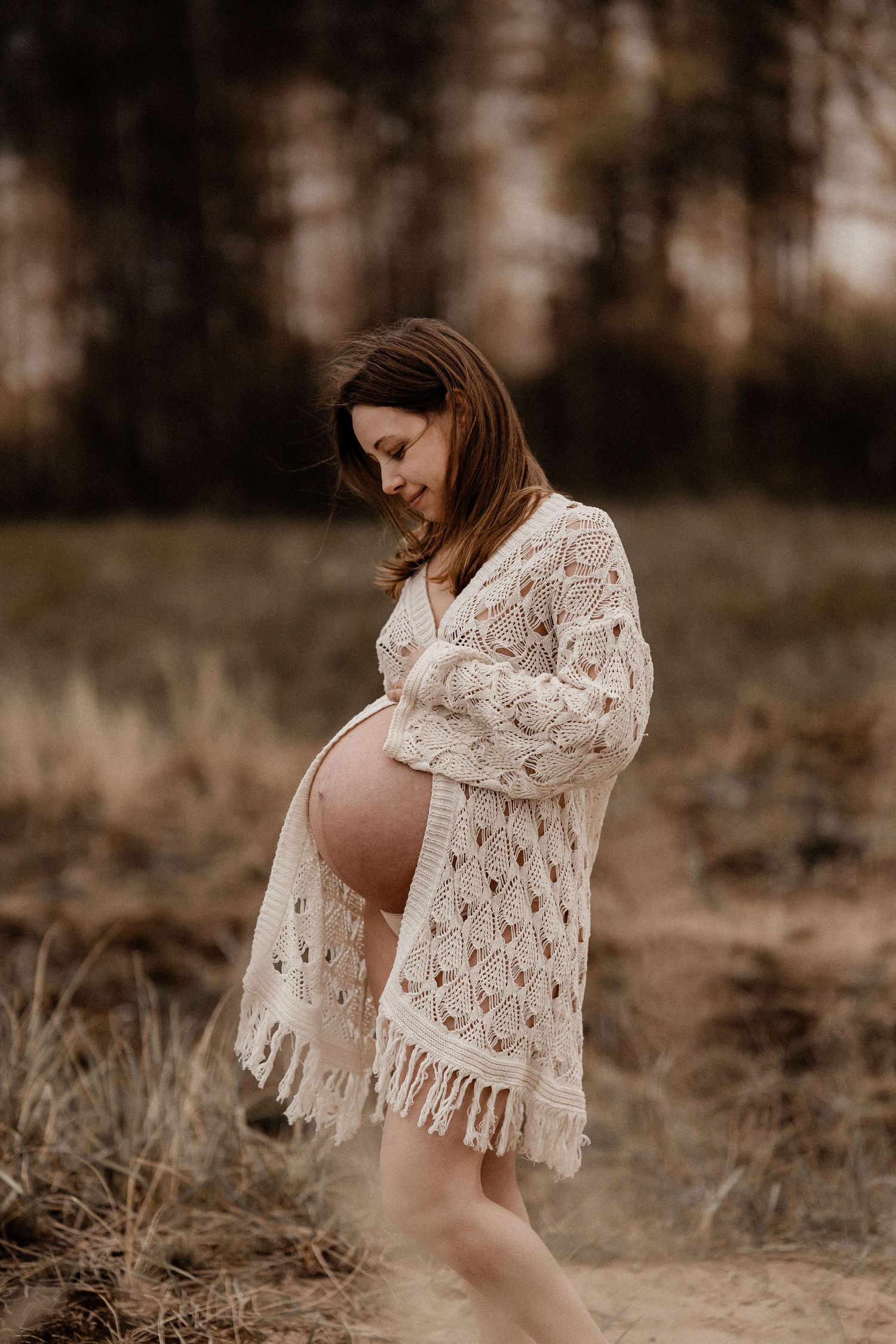 Expecting mother in white crochet dress poses in field during golden hour maternity photoshoot.