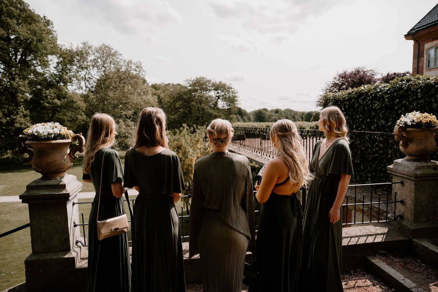 Group stands at stone balustrade overlooking gardens at an elegant outdoor venue.