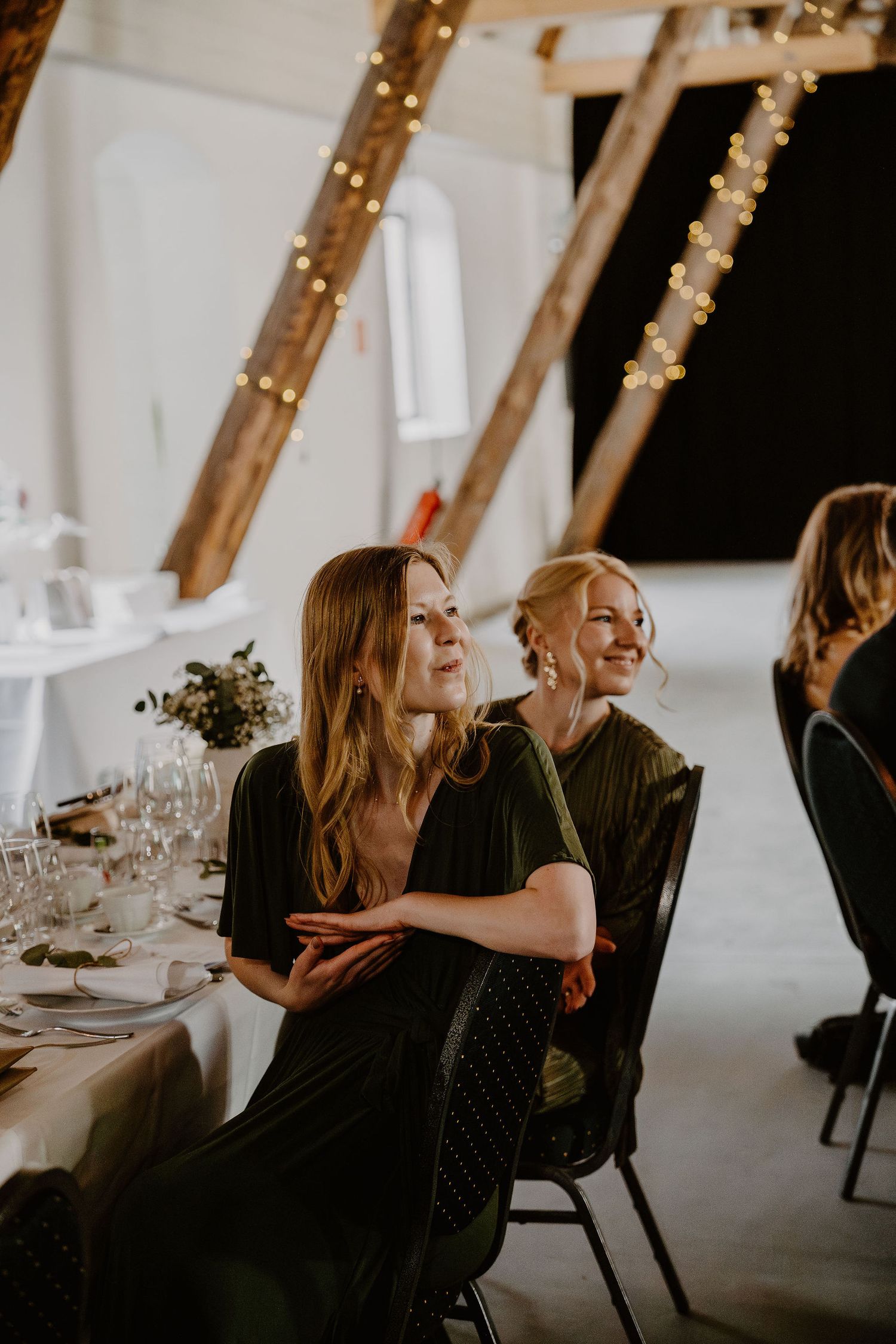 Guests enjoying a candid moment at an elegant reception with twinkling string lights and table settings in background.